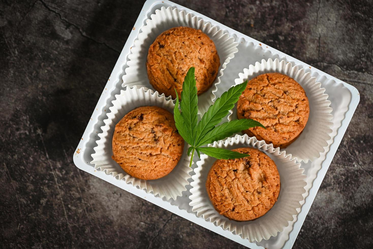 Cannabis food cookies box with cannabis leaf marijuana herb on dark background, delicious sweet dessert cookie with hemp leaf plant THC CBD herbs food snack and medical concept photo