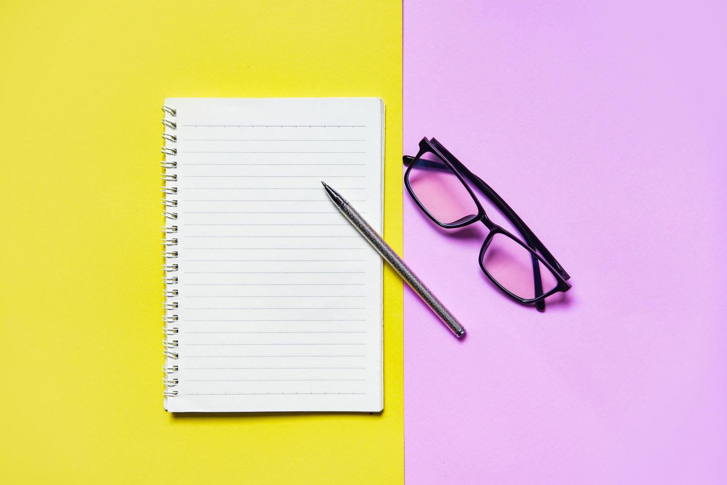 Notepad or notebook paper with pen and glasses on yellow pink for education and business concept photo