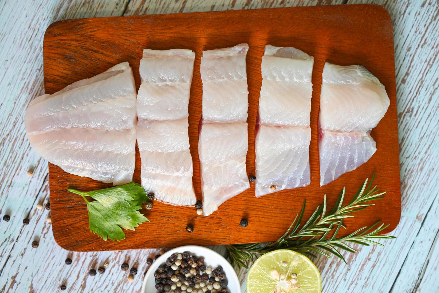 filete de pescado en tabla de madera con ingredientes para cocinar, filete de pescado pangasius crudo fresco con hierbas y especias pimienta negra lima limón y romero, carne dolly pescado tilapia bagre rayado foto