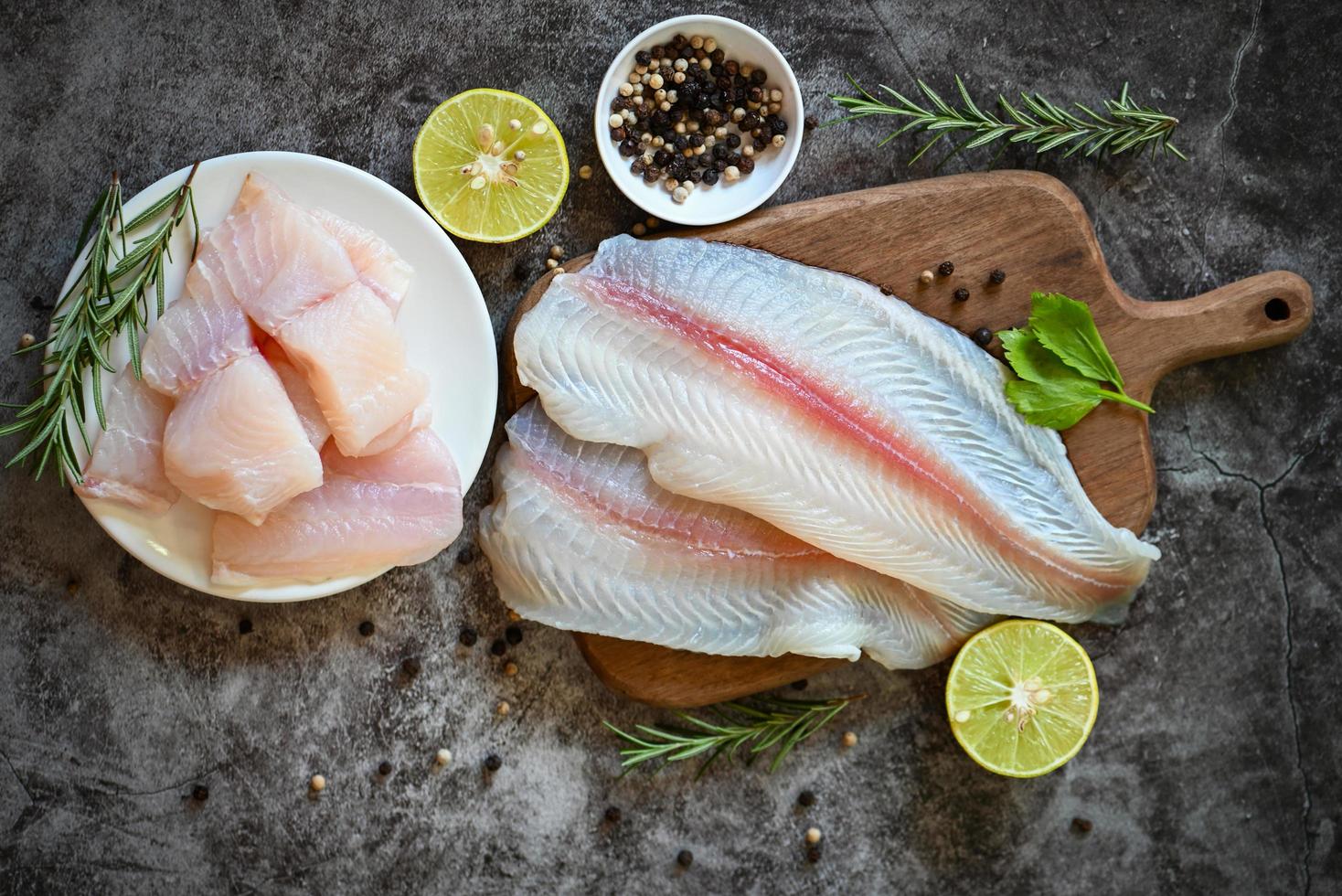 filete de pescado en tabla de madera con ingredientes para cocinar, filete de pescado pangasius crudo fresco con hierbas y especias pimienta negra lima limón, carne dolly pescado tilapia bagre rayado foto