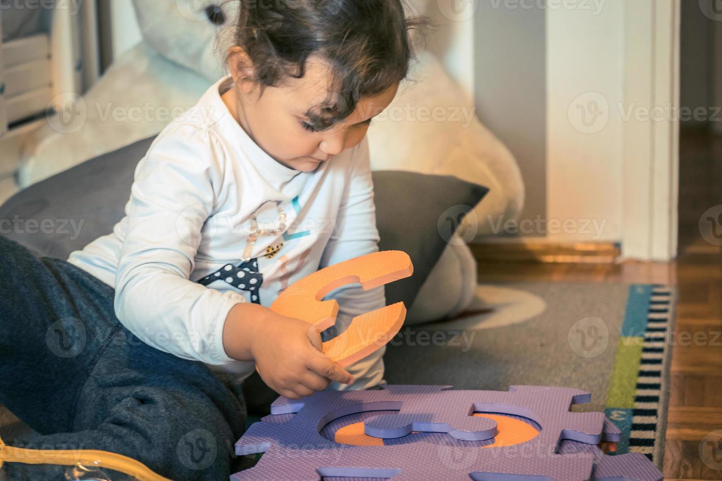 Little girl connecting puzzles on the floor. photo