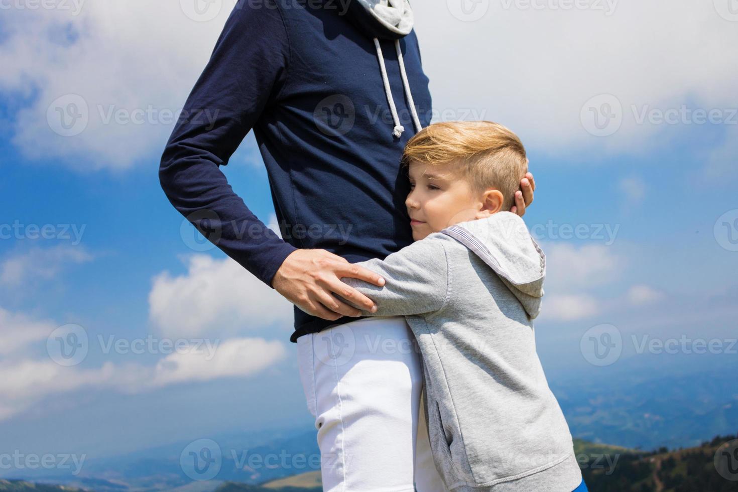 Sad little boy embracing his father against the sky. photo