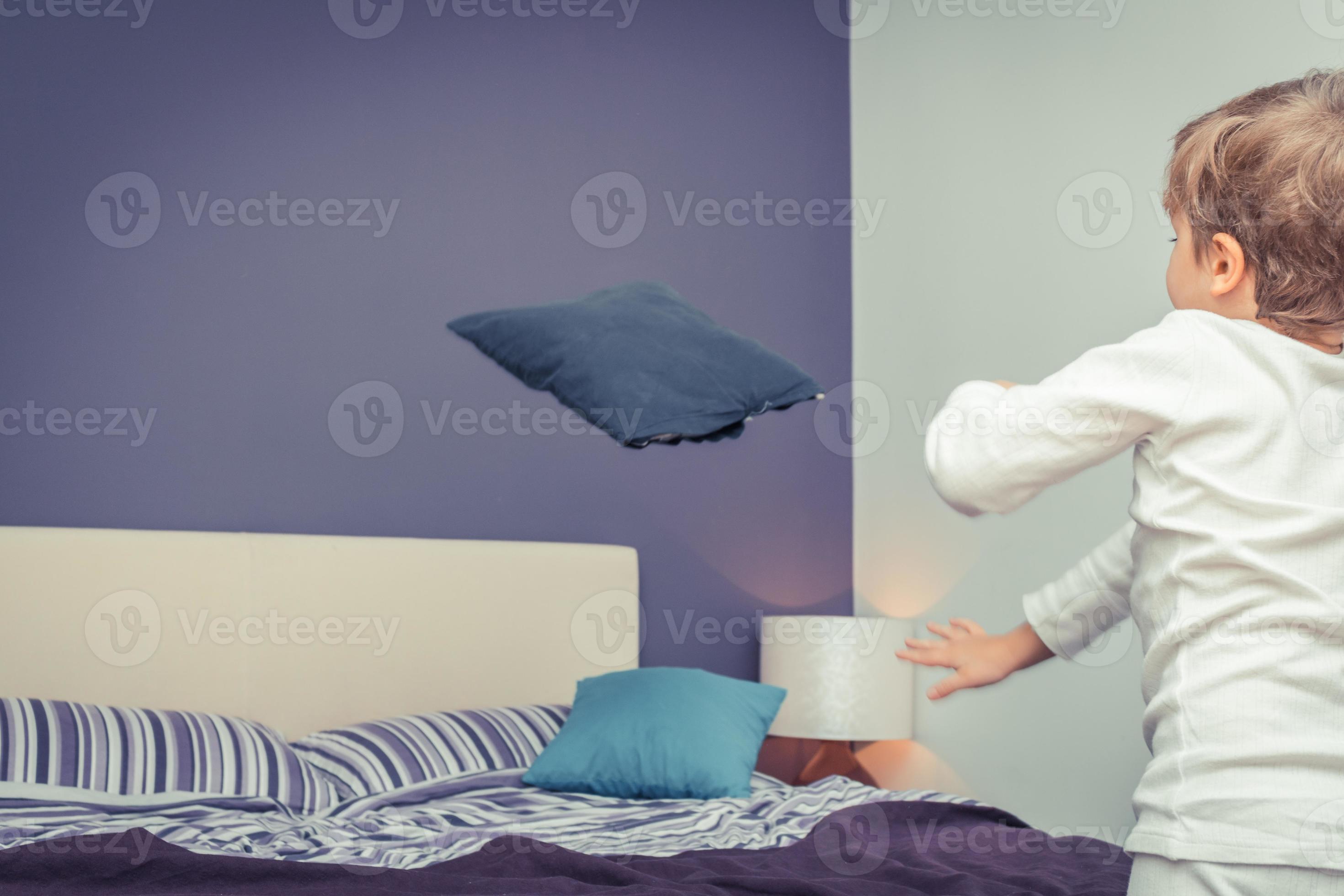 Playful boy throwing pillows in bedroom. 11216997 Stock Photo at Vecteezy