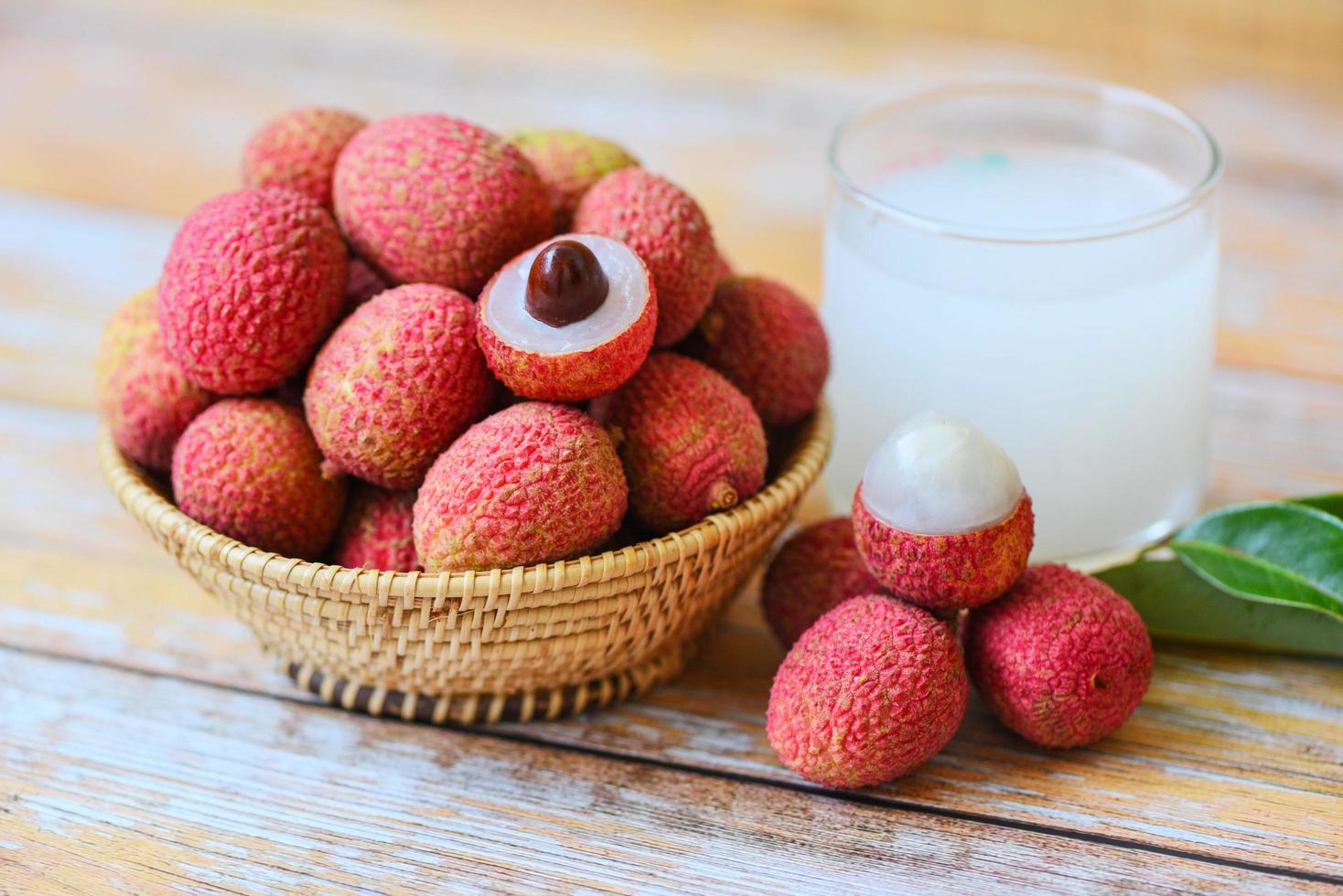 Fresh lychee drink and slice peeled with green leaves harvest in basket from tree tropical fruit summer in Thailand - Lychee juice on wooden table photo