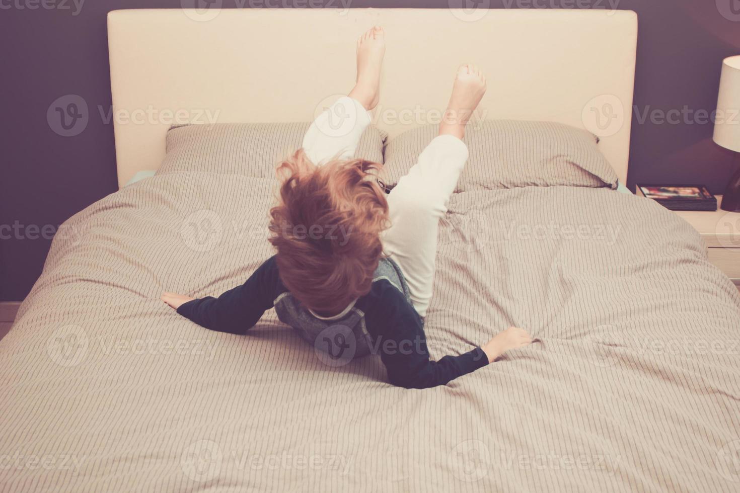 Rear view of boy umping on bed at home. photo