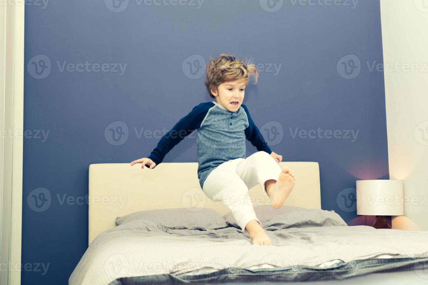 Playful boy in pyjamas jumping on bed. photo