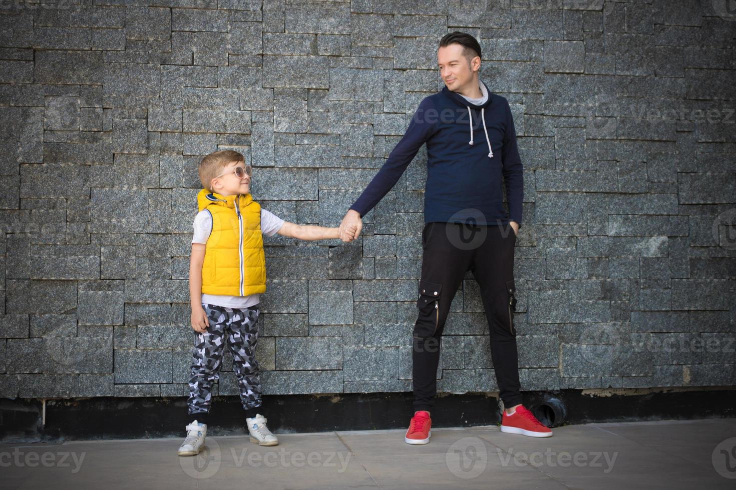 toda la longitud de padre e hijo cogidos de la mano contra la pared. foto