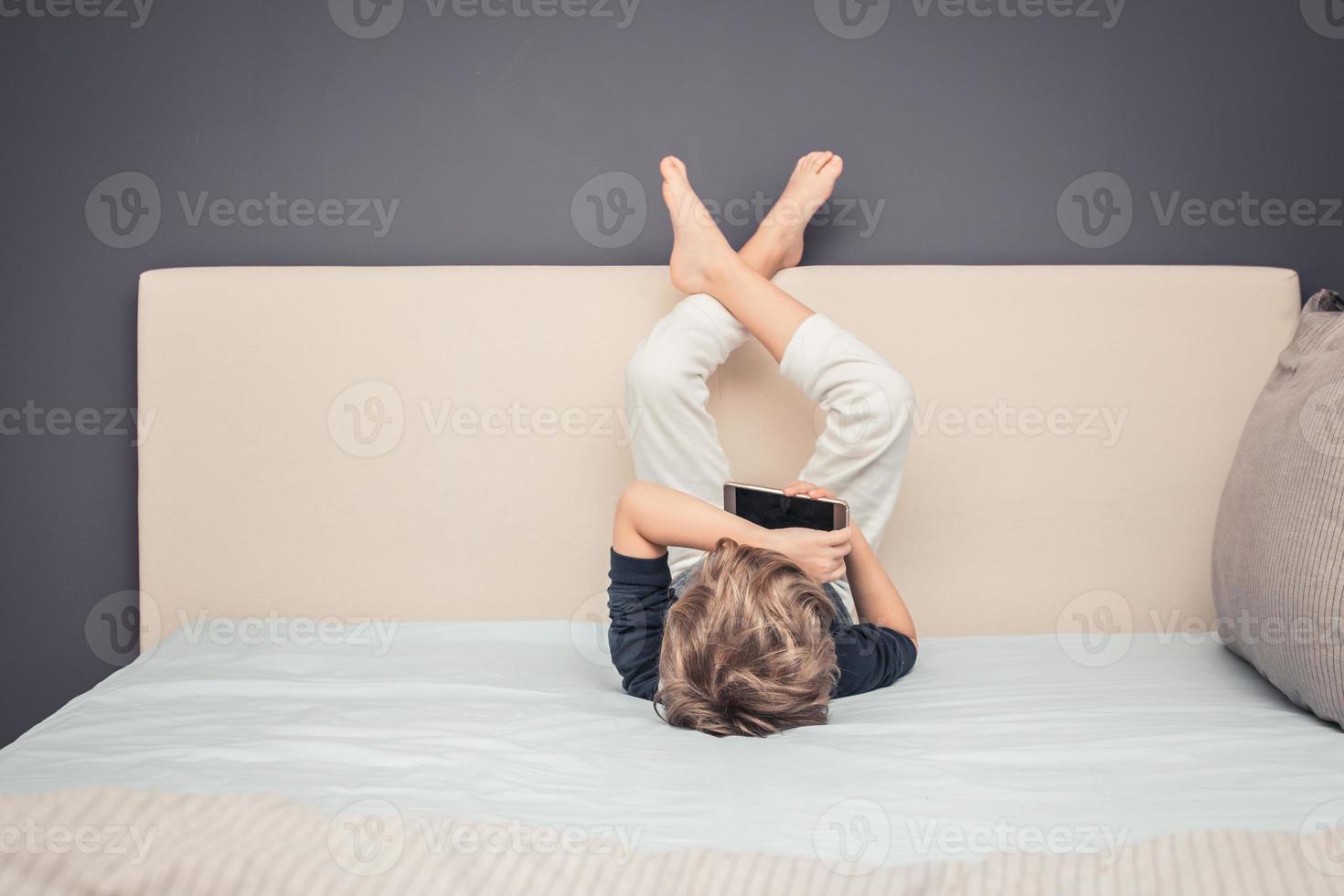 Small boy watching cartoons online while lying on the bed. photo