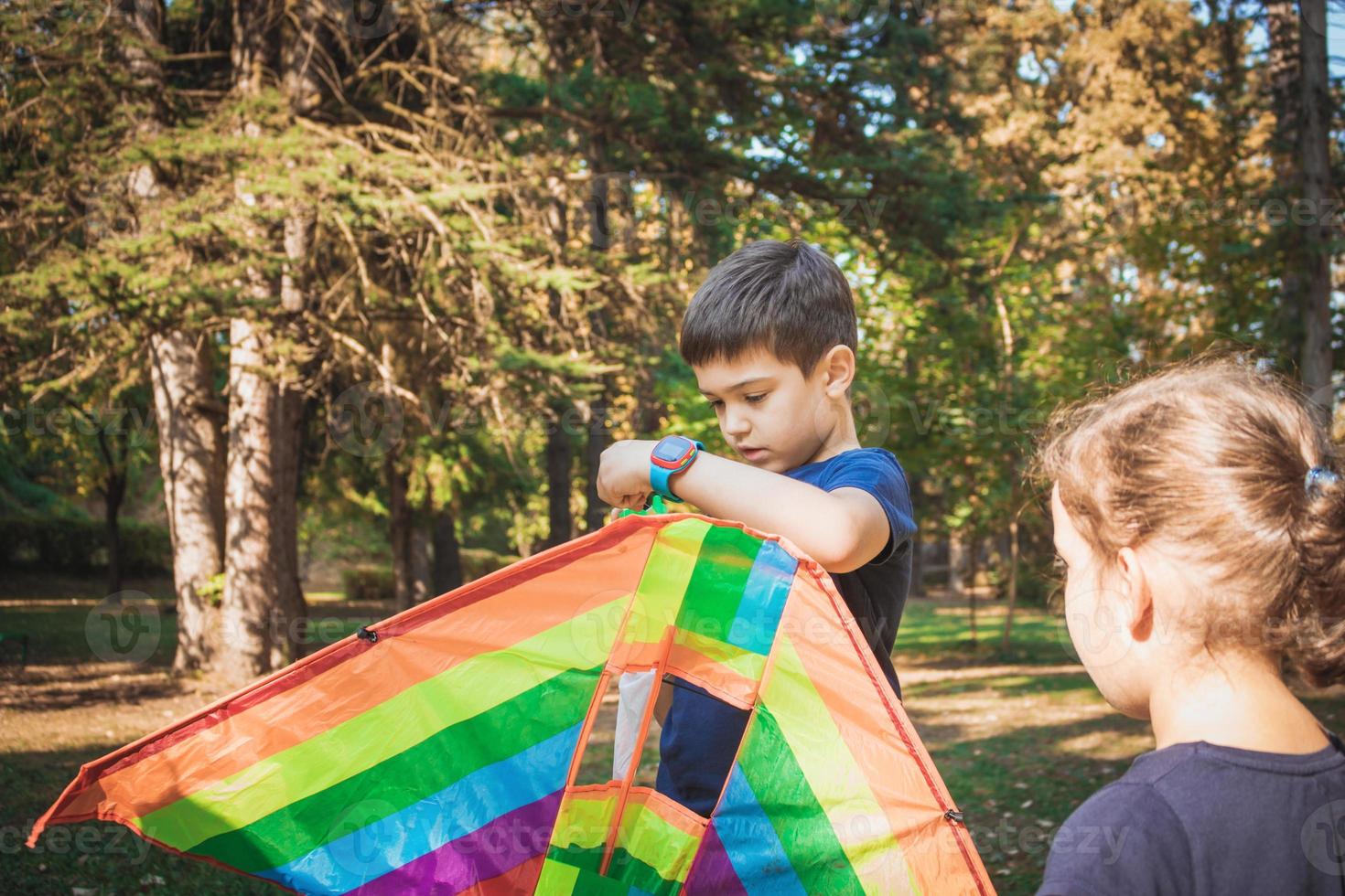 Small boy adjusting kite while playing with sister in nature. photo