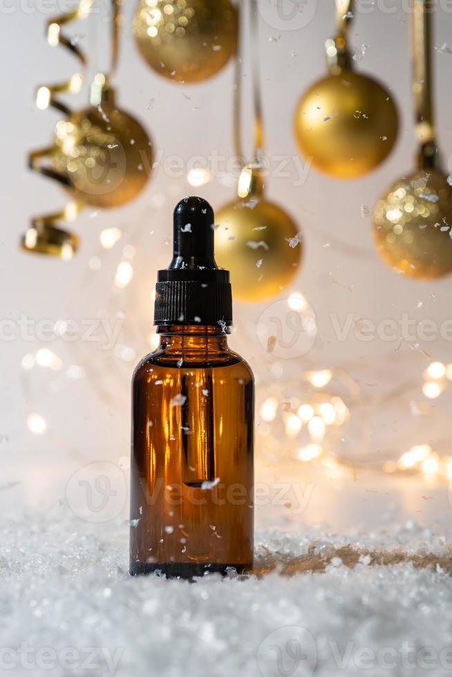 Golden christmas baubles on the glitter shiny background. Cosmetic container with dropper and serum. New year cosmetics concept. photo
