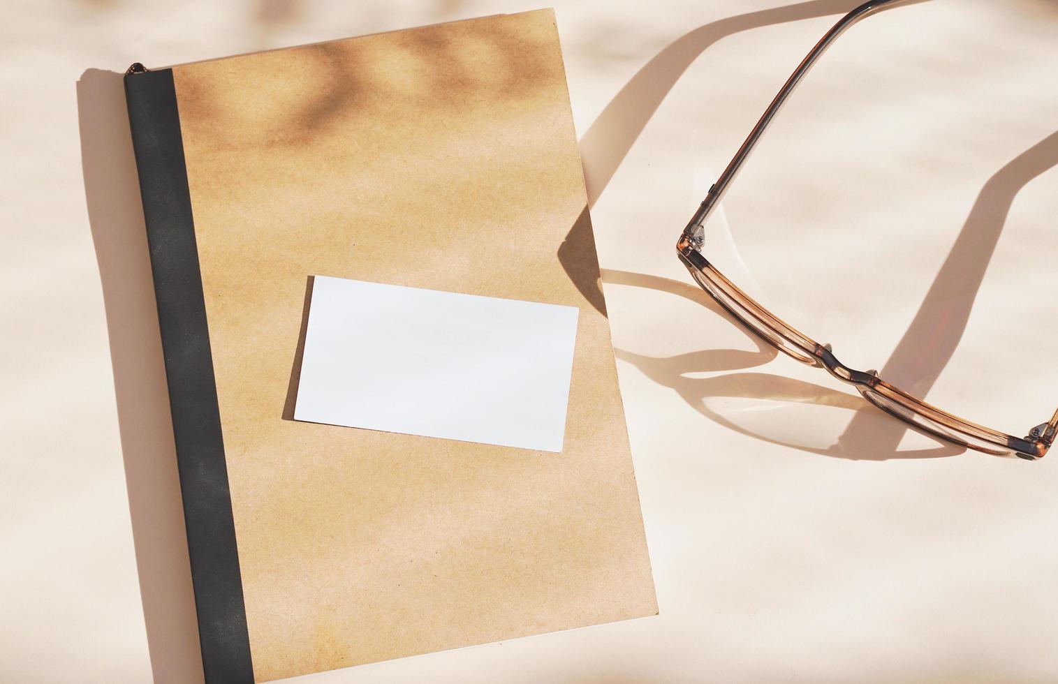 Flat lay of branding identity business name card on notebook with eyeglasses, light and shadow shape leaves, minimal concept for design photo