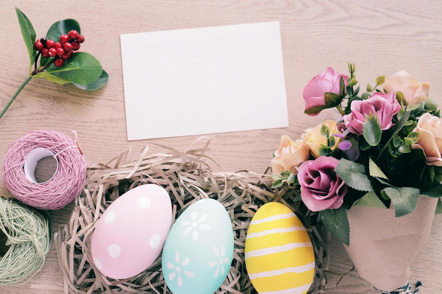 Pastel and colorful easter eggs in nest and bouquet of flower with blank card on wooden background, happy easter holiday concept photo