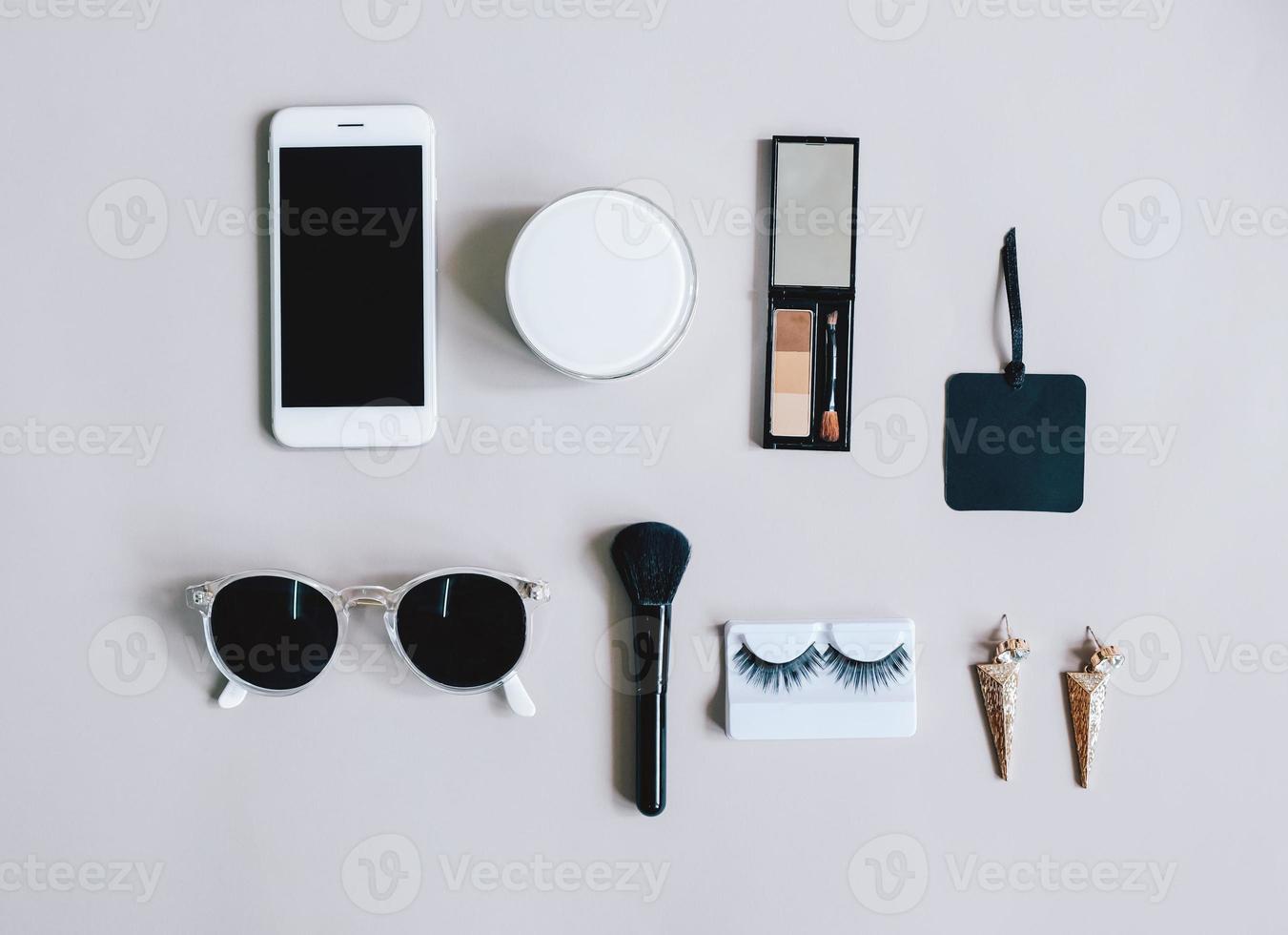Fashion concept Flat lay of feminine items with cosmetics and accessories with smartphone on grey background, top view with minimal style photo