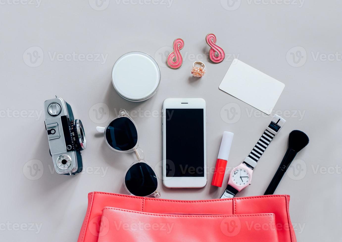 Flat lay of pink leather woman bag open out with cosmetics, accessories, tag card and smartphone on grey background with copy space photo