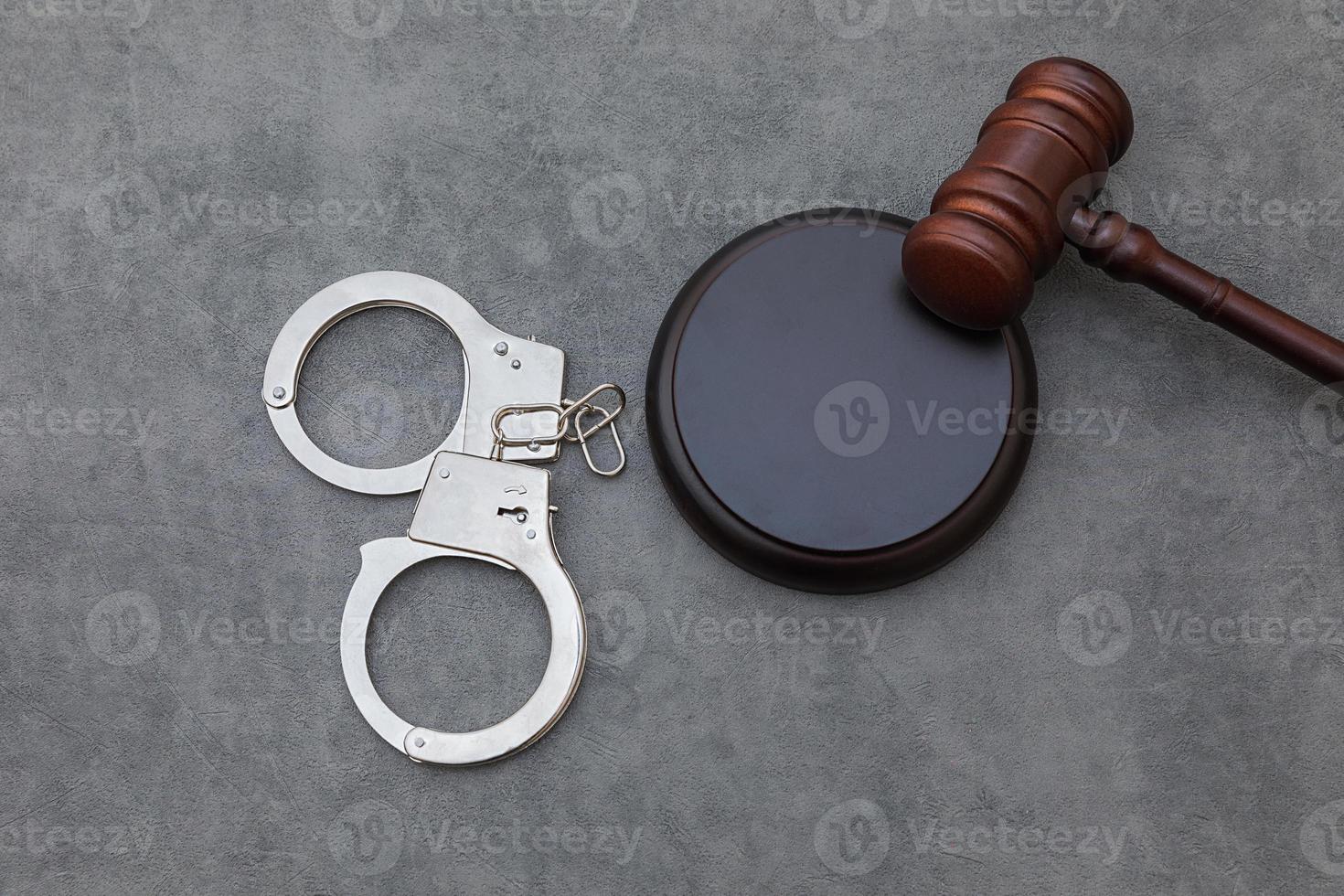 Law theme. Court of law trial in session. Judge gavel handcuffs on grey table in lawyer office or court session. Mallet of judge on concrete stone grey background. Justice human rights concept. photo