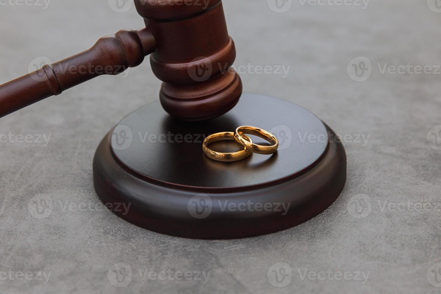 Law theme. Judge gavel wedding rings on concrete stone grey background. Divorce proceedings. Mallet of judge deciding on marriage divorce, marital agreement, legalities of divorce. photo