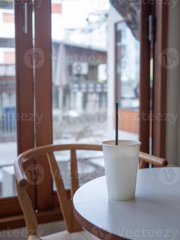 ice milk coffee in white plain empty paper cup on table near glass window in minimal japanese style cafe photo