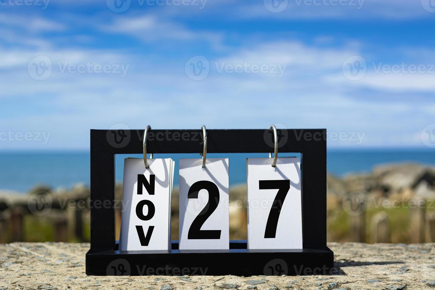 Nov 27 calendar date text on wooden frame with blurred background of ocean. photo