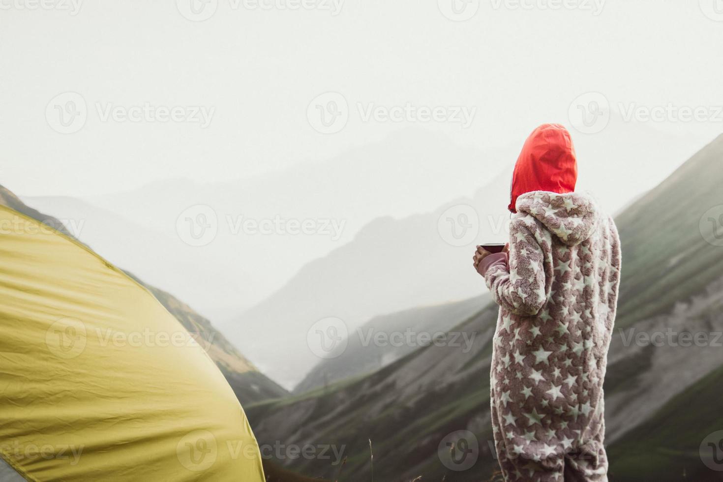 BAck view Woman dreamy in jumpsuit stand with mug of coffee wild camping outdoors enjoy carefree lifestyle think about life. Nature lover hipster wanderer wanderlust photo