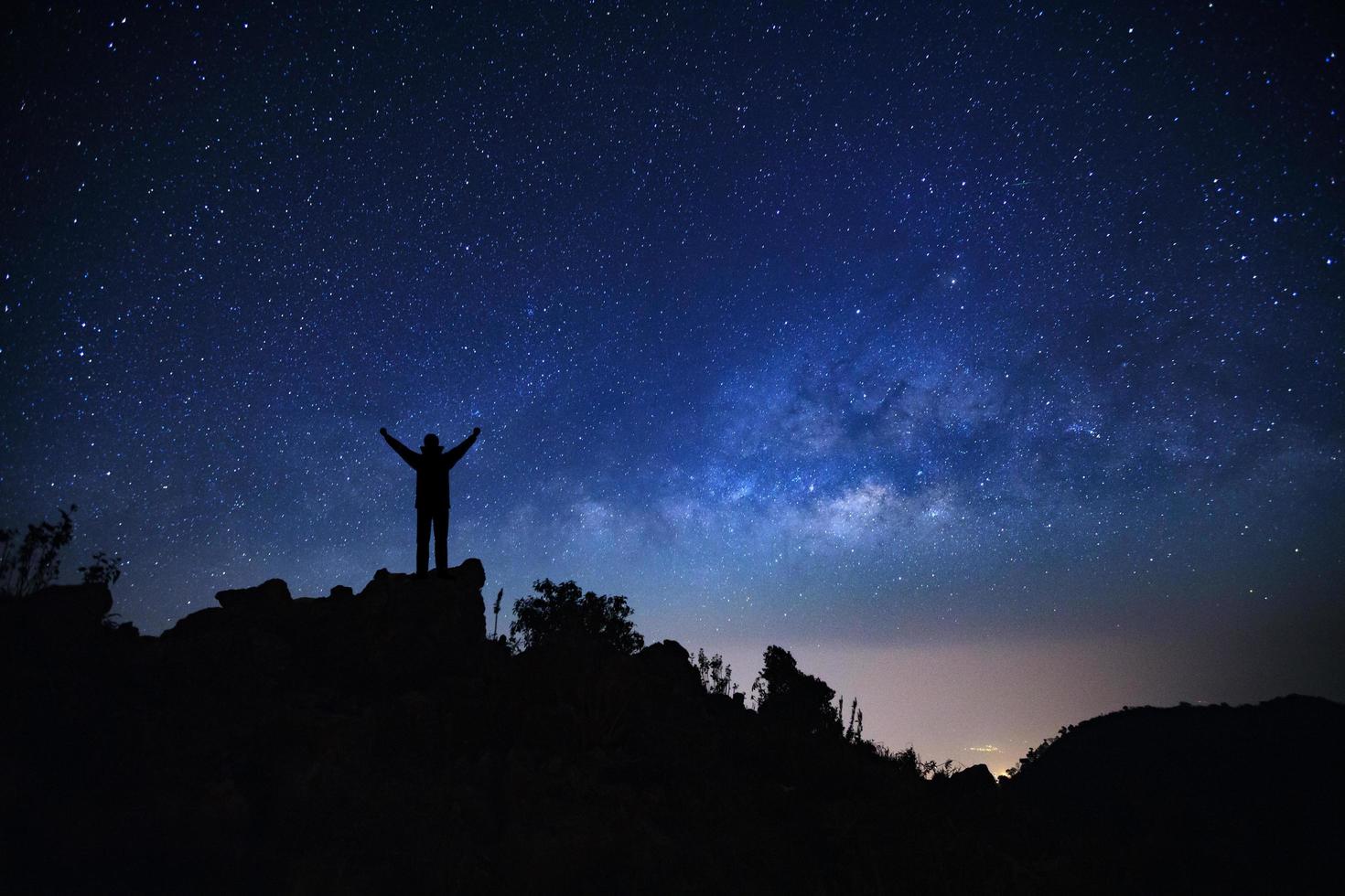 paisaje con galaxia de la vía láctea, cielo nocturno estrellado con estrellas y silueta de un hombre deportivo de pie con los brazos levantados en la alta montaña. foto