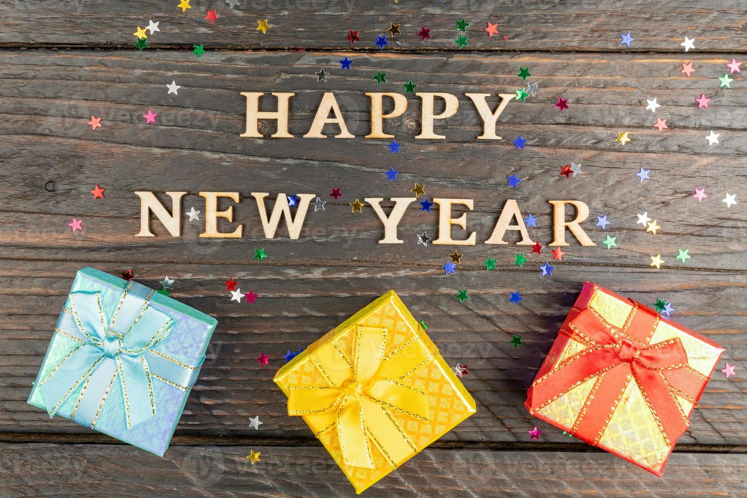 feliz año nuevo 2023. cita hecha de letras de madera sobre fondo de madera con pequeñas cajas de regalo multicolores. concepto creativo para la tarjeta de felicitación de año nuevo foto