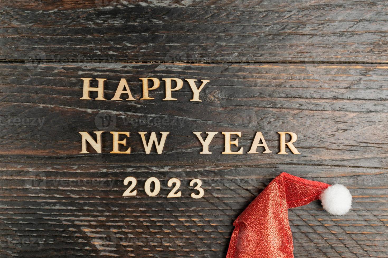 Happy new year 2023 greeting card. Quote madeof wooden letters on wooden background with red Santa hat. Festive background photo