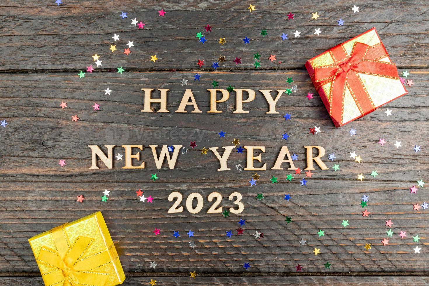 Happy new year 2023 next and red and yellow small gift boxes on dark wooden background with confetti. photo