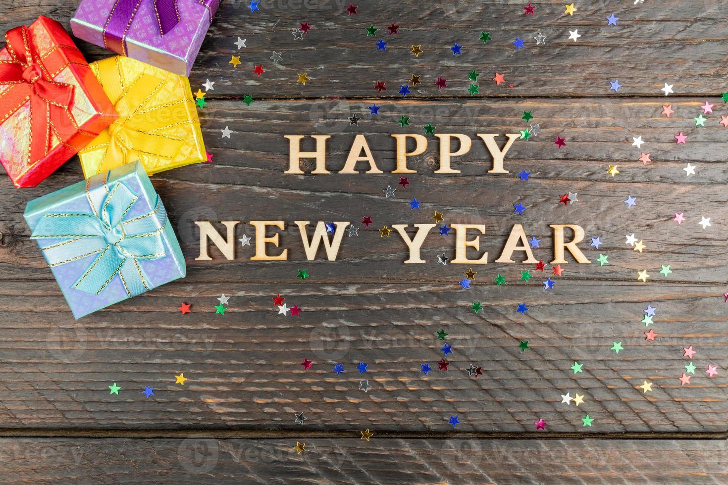 tarjeta de felicitación festiva creativa con texto de madera feliz año nuevo y pila de cajas de regalo brillantes con regalos. copiar espacio para texto foto
