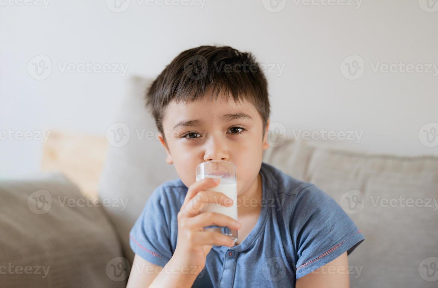 Portrait healthy school boy drinking glass of milk for breakfast, Happy child sitting on sofa drinking warm milk before go to school. healthy food lifestyle concept photo
