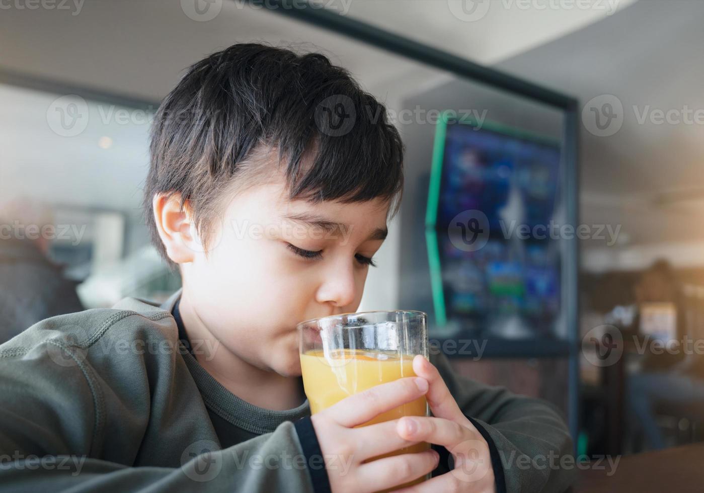 Portrait Young kid drinking fresh orange juice for breakfast in cafe, Happy child boy drinking glass of fruit juice while waiting for food in restaurant, Healthy food lifestyle concept photo