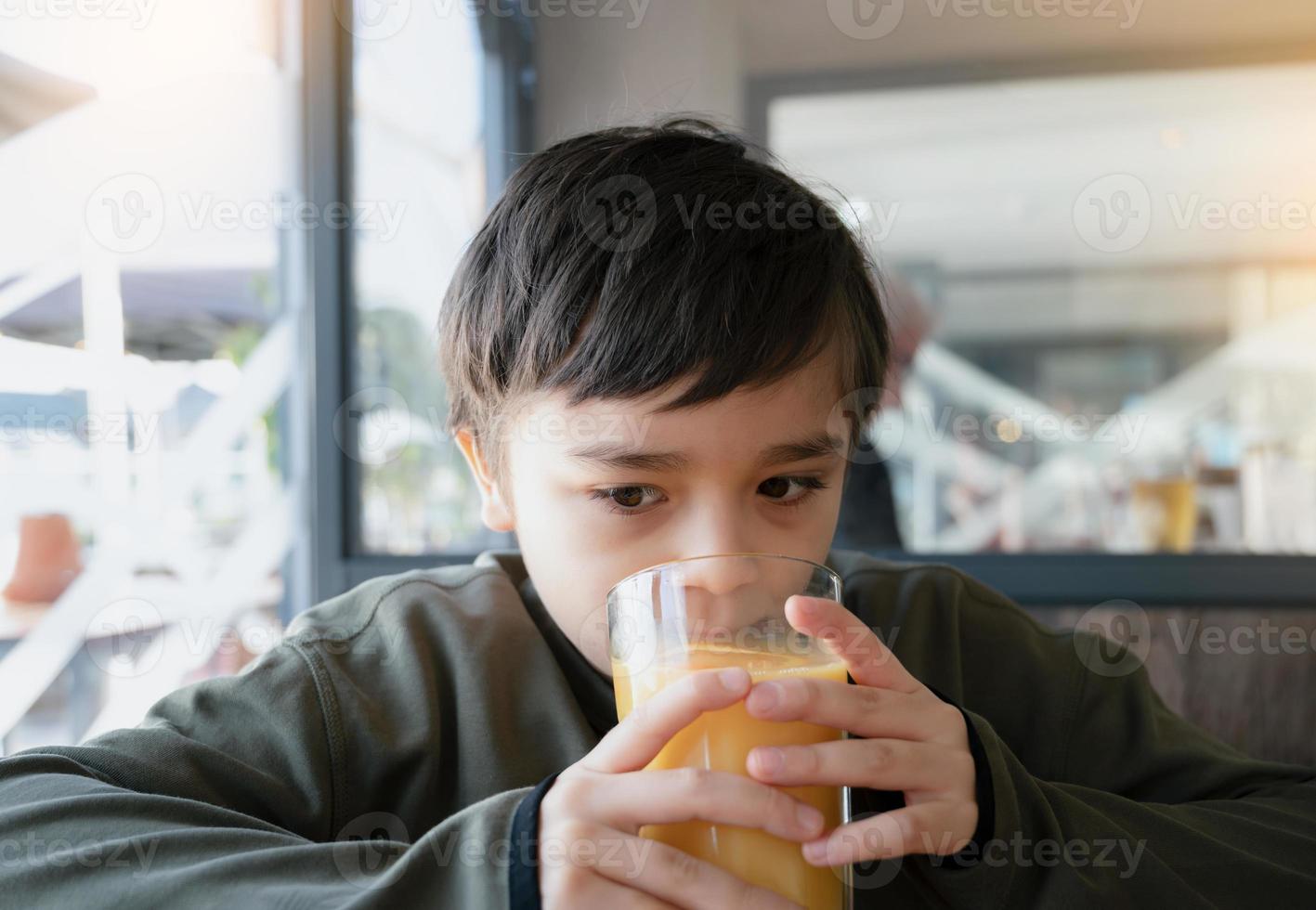 Portrait Young kid drinking fresh orange juice for breakfast in cafe, Happy child boy drinking glass of fruit juice while waiting for food in restaurant, Healthy food lifestyle concept photo
