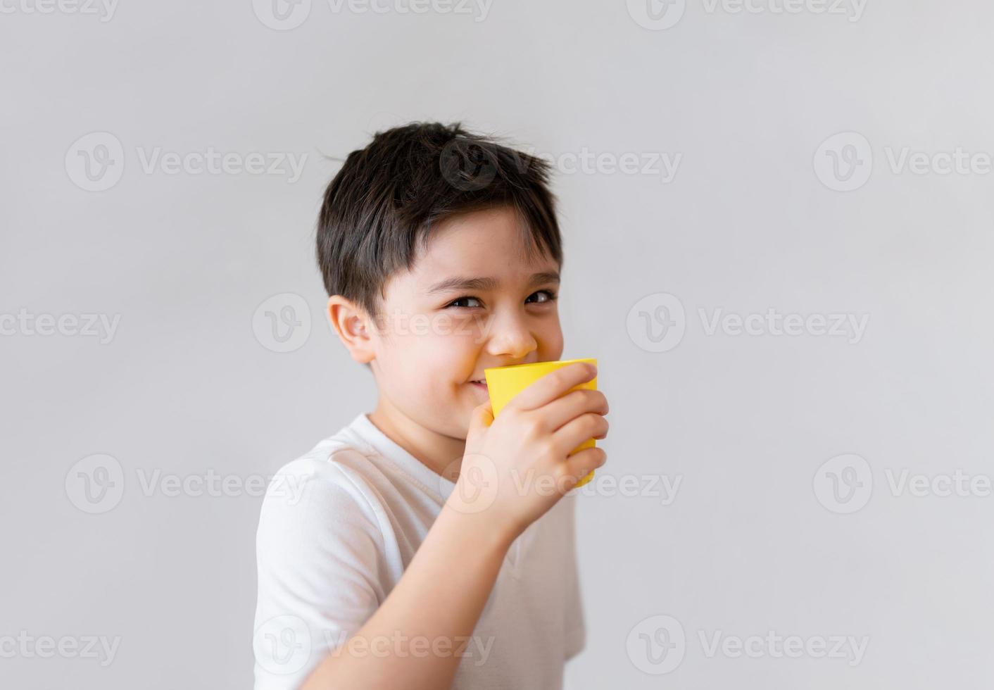 Portrait Young kid drinking fresh orange juice for breakfast, Isolated Happy child boy drinking glass of fruit juice and looking at camera with smiling face, Healthy kids food lifestyle concept photo