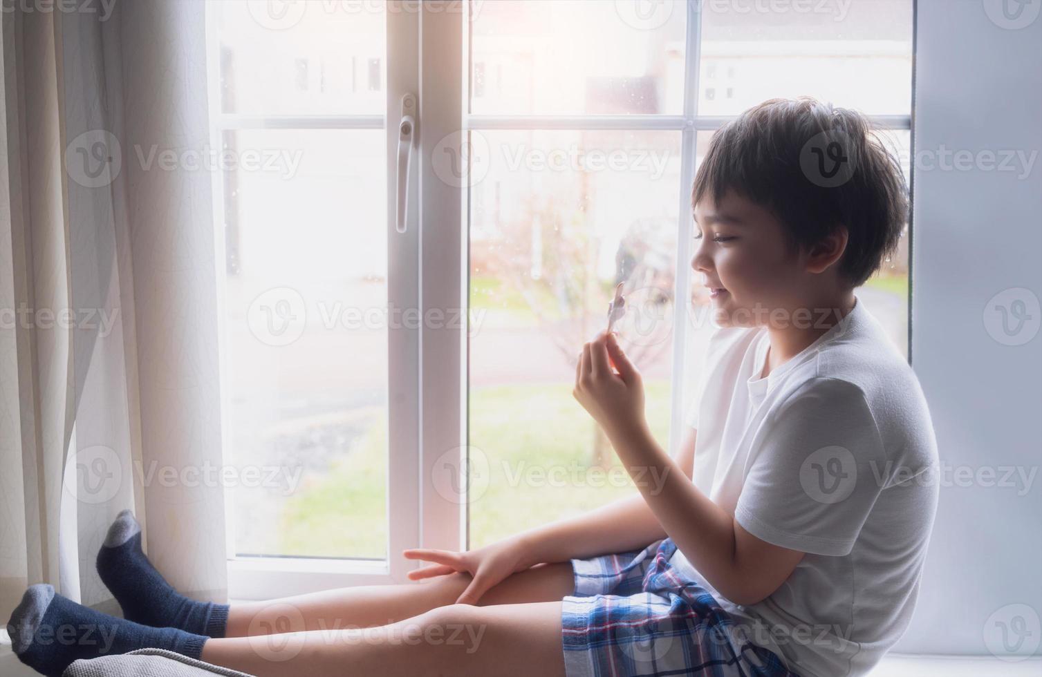 A Happy kid eating some ice cream, Portrait of a handsome young boy sitting next to a window having a refreshment, Child with a smiling face relaxing at home. Kid looking at camera photo