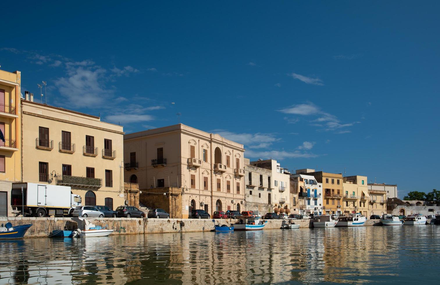 The banks of the Mazaro River in Mazara del Vallo, Italy. The houses are reflected in the water. In the background the blue sky with small white clouds. photo