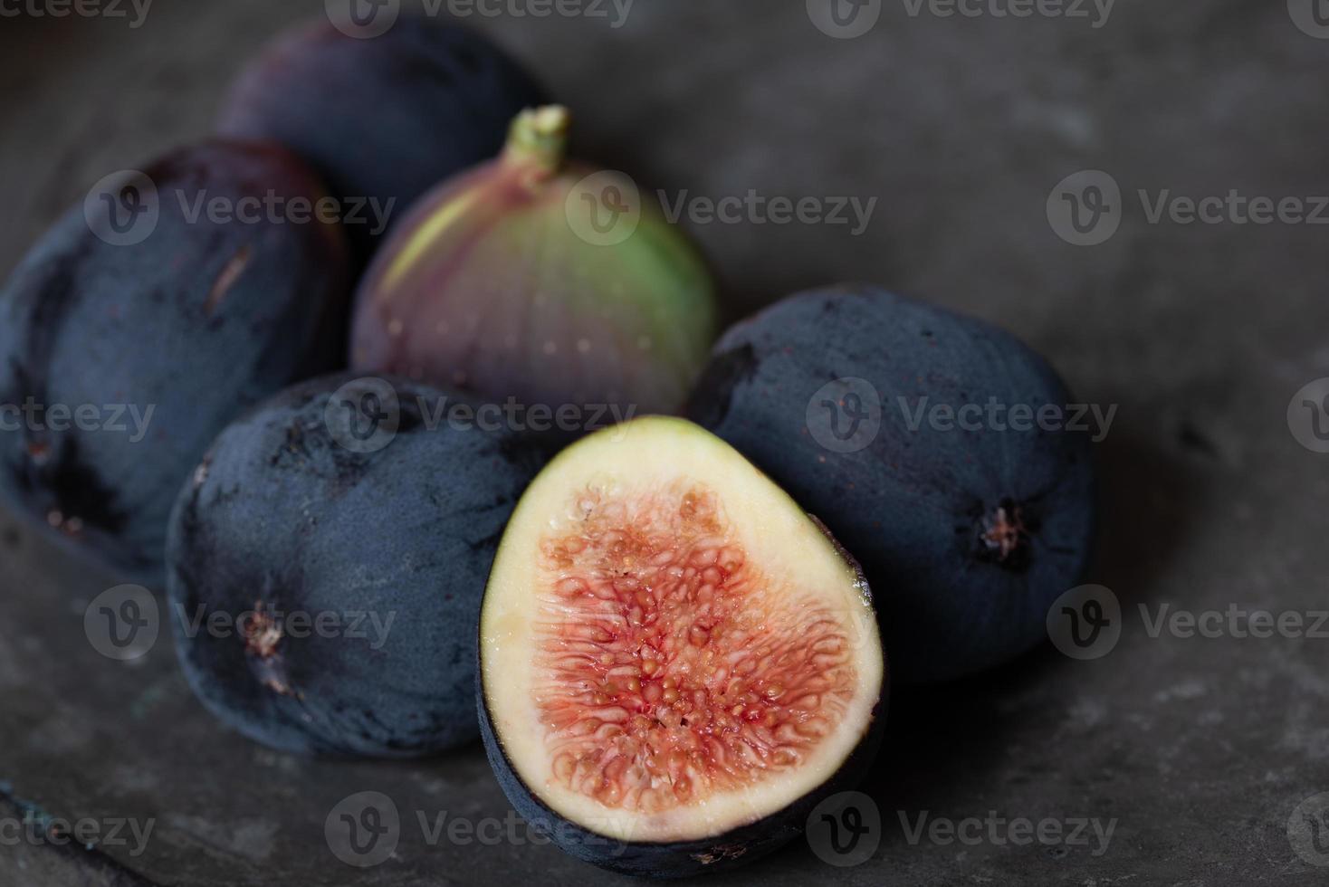 Close up of several dark figs lying on an old metal plate. A fig is cut open. photo