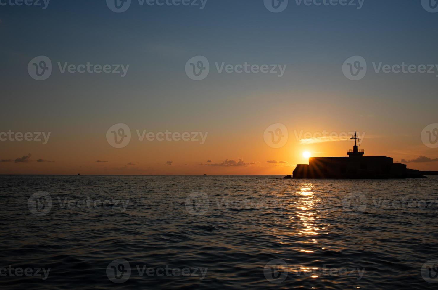 el sol se pone en el mar. el cielo brilla azul y naranja. la luz se refleja en las ondas. la sombra de una torre de señales está frente al sol al costado de la imagen. foto