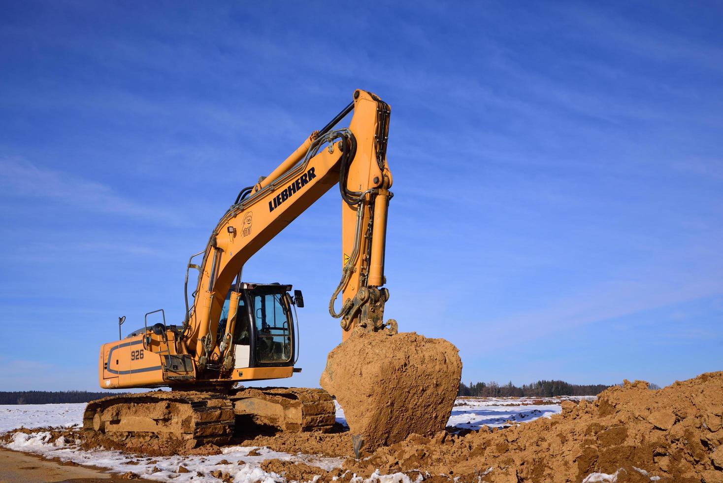 A yellow shovel excavator stands in winter near Augsburg, against a blue sky, on loamy soil. A lot of clay sticks to the excavator shovel. photo