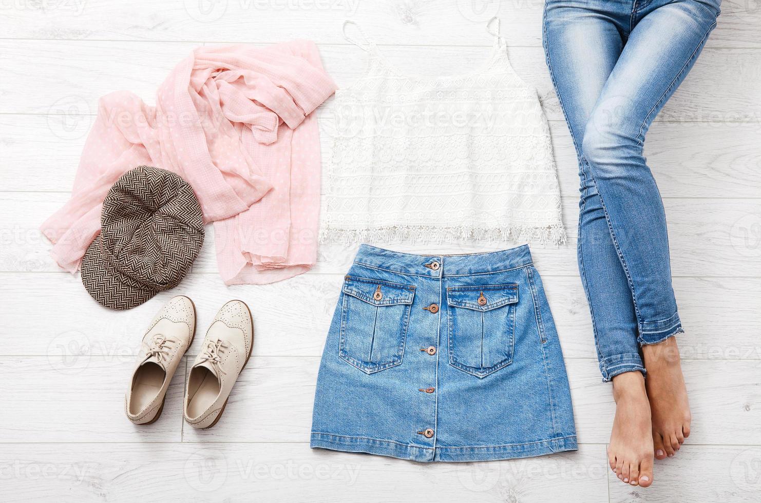 Casual summer outfit with different accessories and female legs in jeans on white wooden floor. Top view and copy space. photo