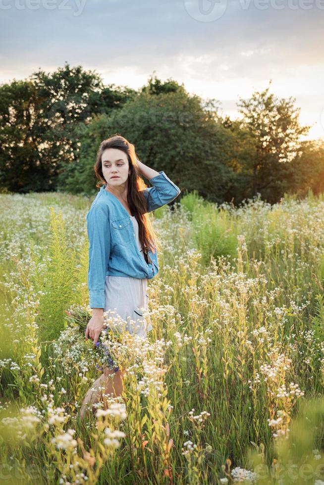 hermosa chica caminando en el campo en verano con flores silvestres. foto