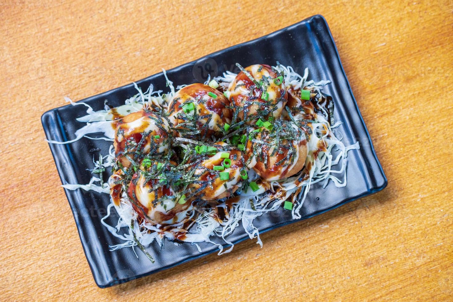 Octopus Fillet Takoyaki Garnish with seaweed. chopped white cabbage and scallions in a black dish, Saimoden, circled on a wooden table photo
