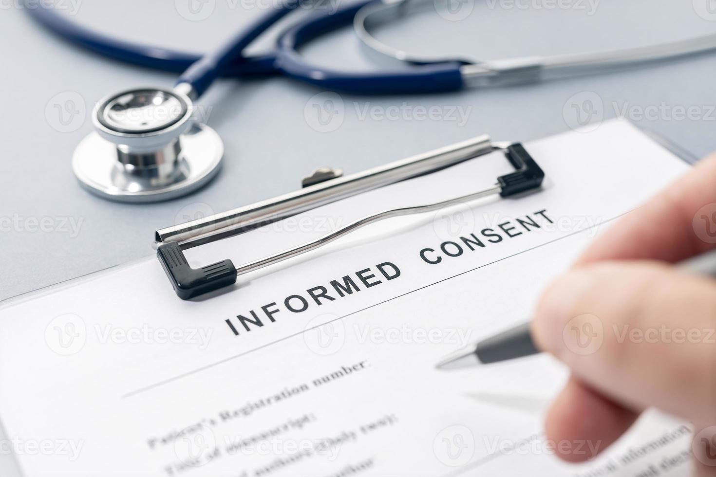 Hand filling a Informed Consent form and stethoscope on desk photo