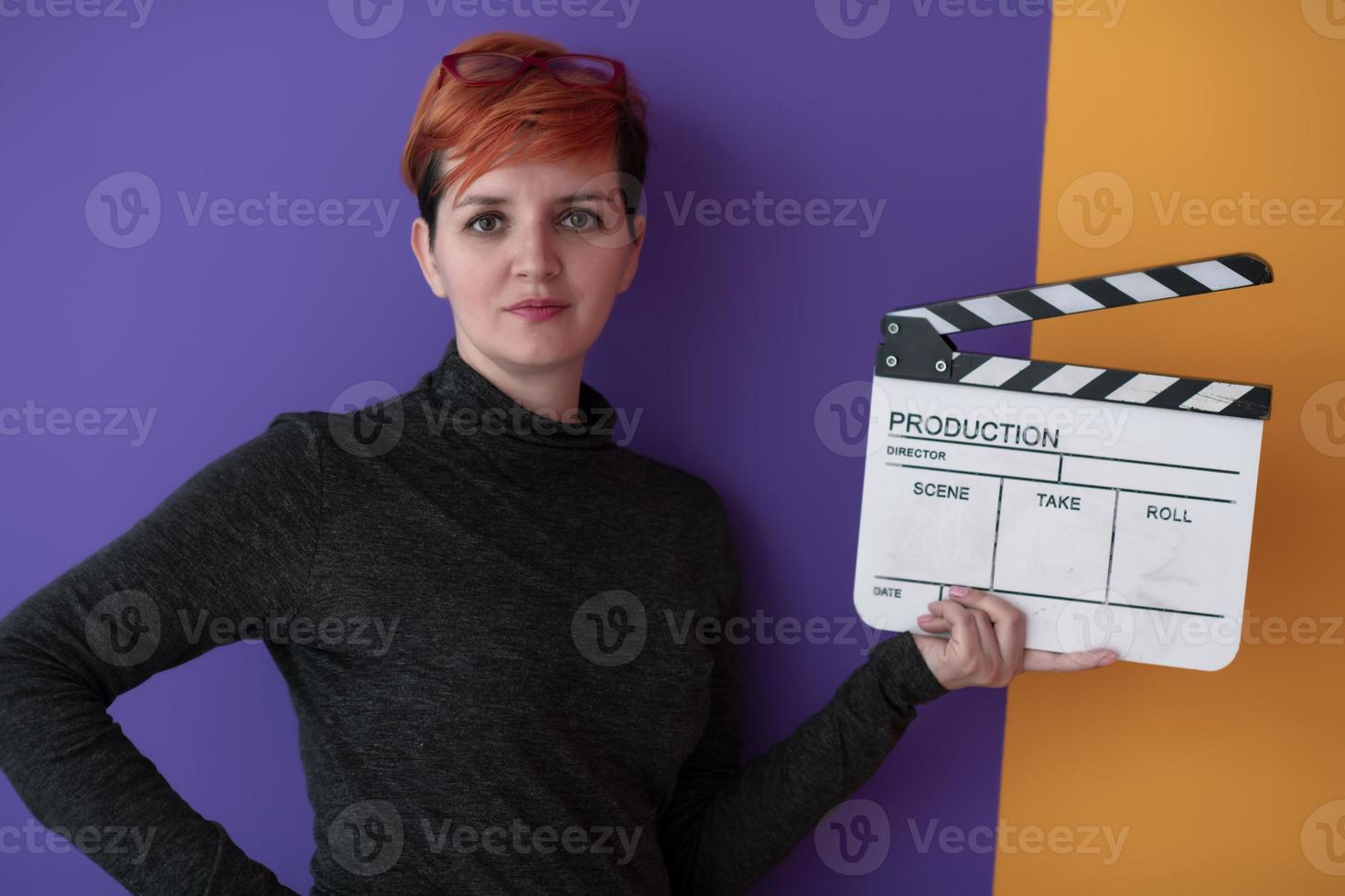 mujer pelirroja sosteniendo la chapaleta de la película sobre fondo púrpura foto