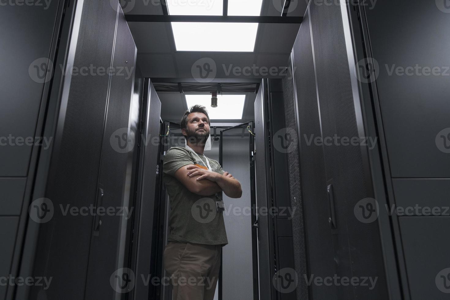 Portrait of male technician or network administrator standing brave as a hero with arms crossed in data center server room. photo