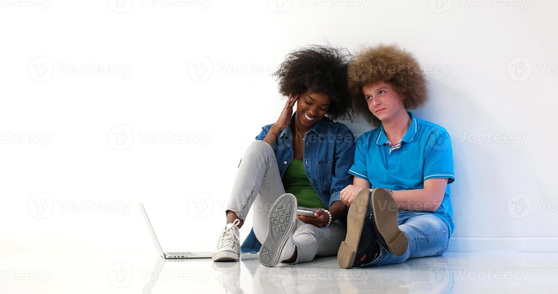 multiethnic couple sitting on the floor using a laptop and tablet photo