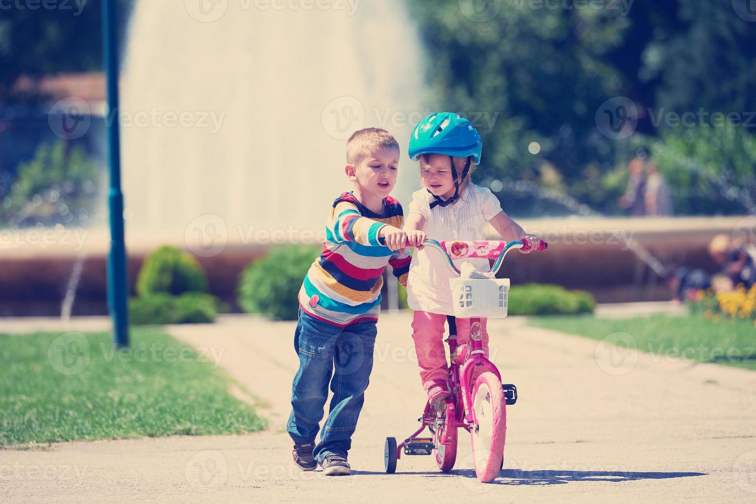 Boy and girl in park learning to ride a bike photo