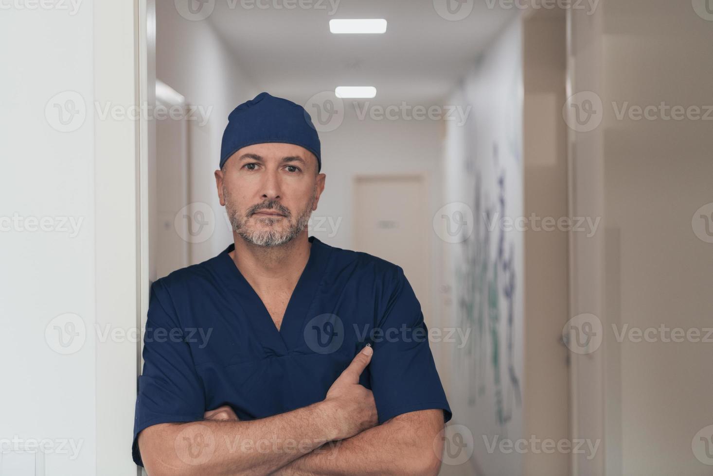 Portrait Of Mature Male Doctor In Busy Modern Hospital Corridor. photo