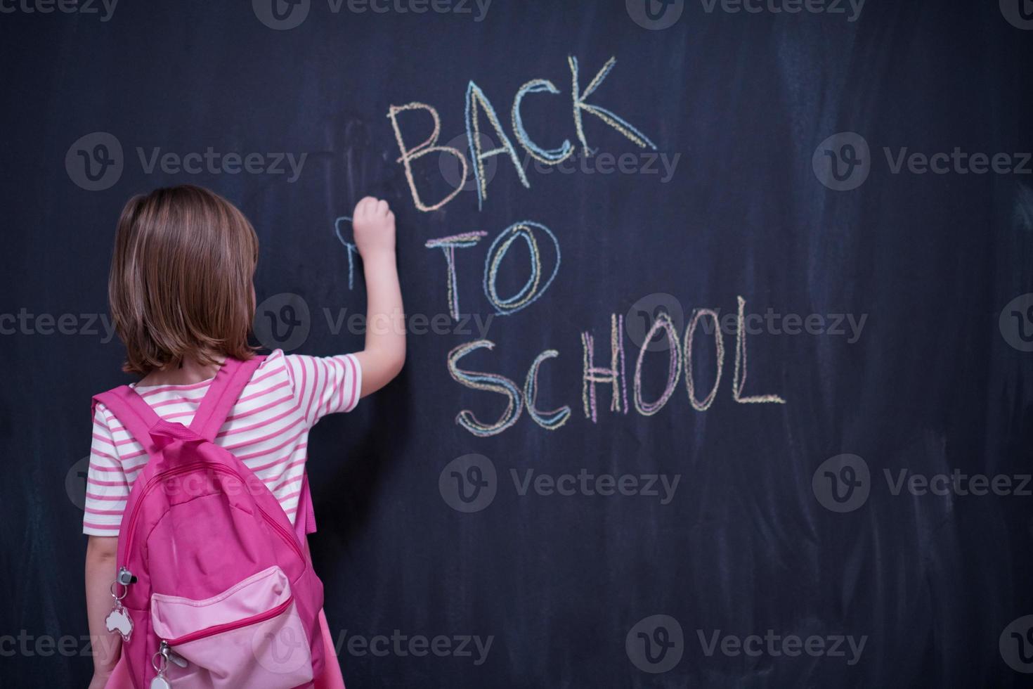 school girl child with backpack writing  chalkboard photo