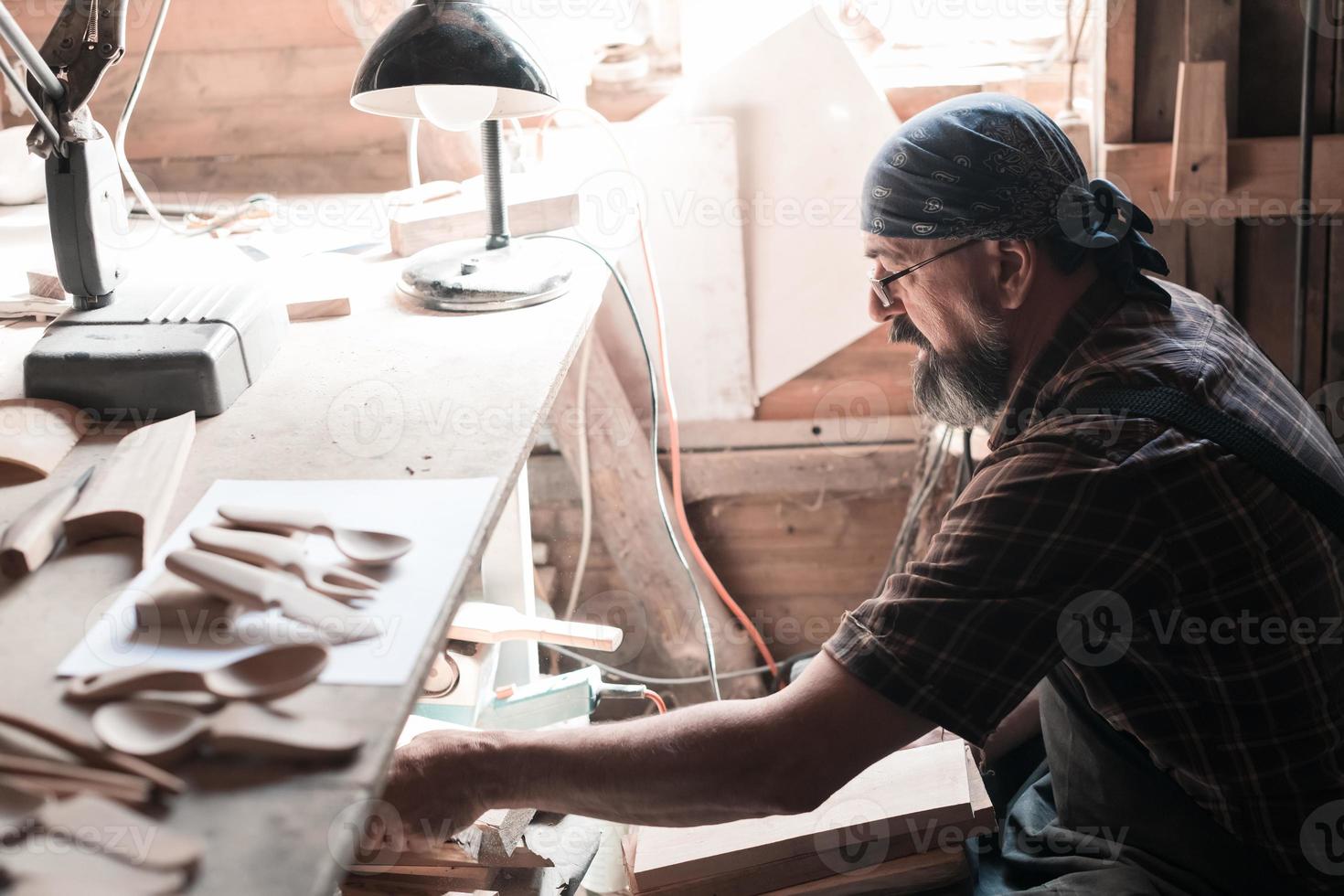 maestro de cucharas en su taller con productos de madera y herramientas seleccionando la madera adecuada para fabricar productos de cocina de madera. foto