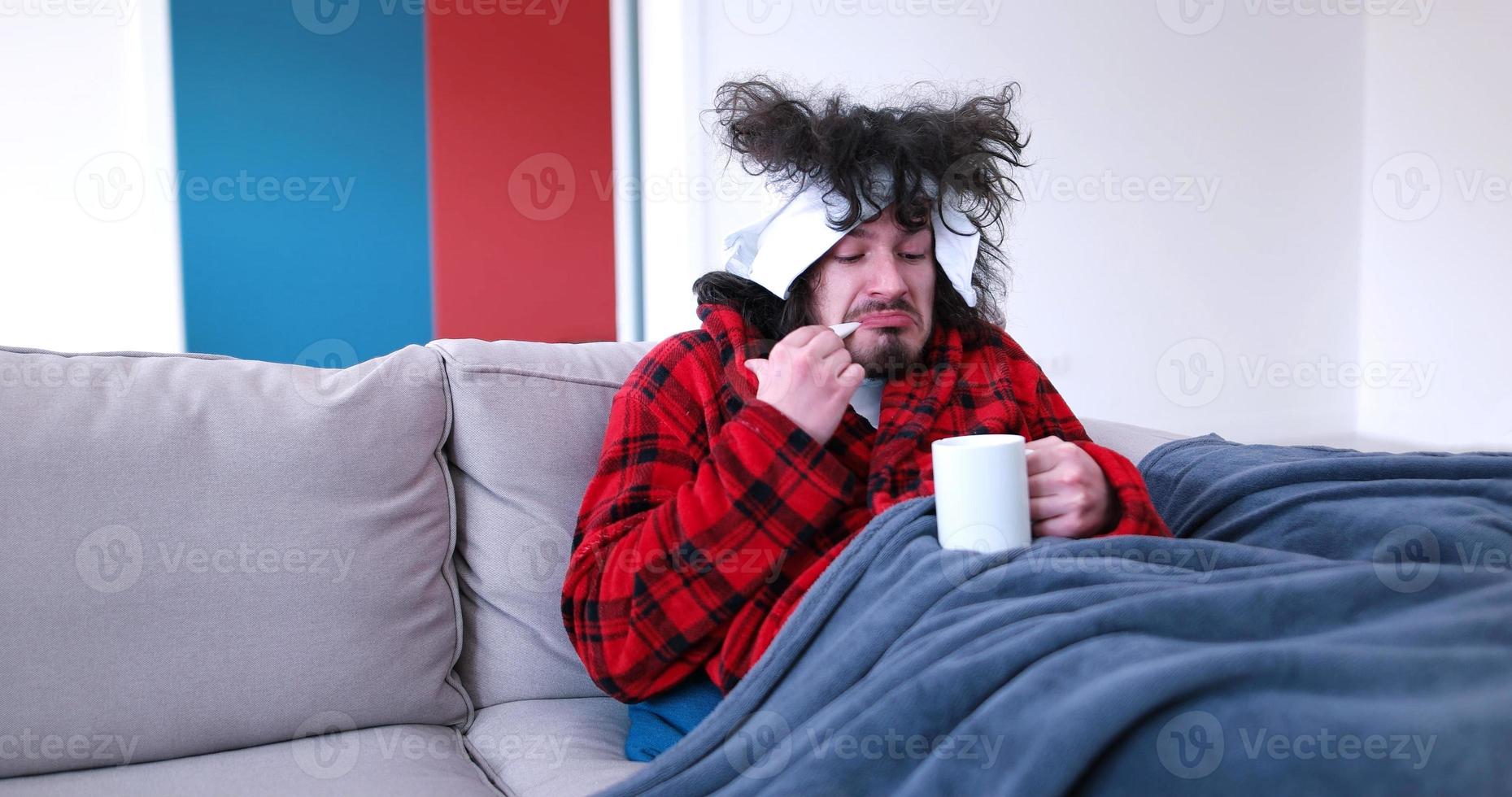 sick man is holding a cup while sitting on couch photo