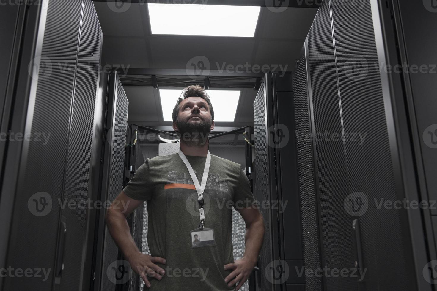 Portrait of male technician or network administrator standing brave as a hero with arms crossed in data center server room. photo